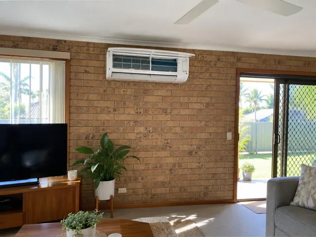 Open split system on a brick internal wall in a living room with a sliding door and ceiling fan in Labrador