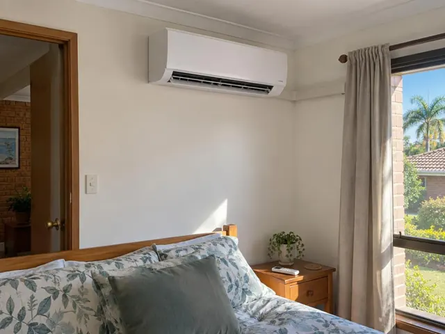 Wall-mounted split system above a bed in a bedroom with curtains and a window in Parkwood