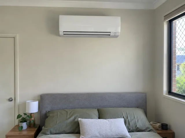 Wall-mounted split system above a bed in a light bedroom with window and side tables in Southport